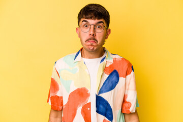 Young caucasian man isolated on yellow background shrugs shoulders and open eyes confused.