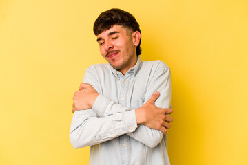 Young caucasian man isolated on yellow background hugs, smiling carefree and happy.