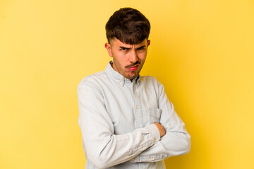 Young caucasian man isolated on yellow background frowning face in displeasure, keeps arms folded.