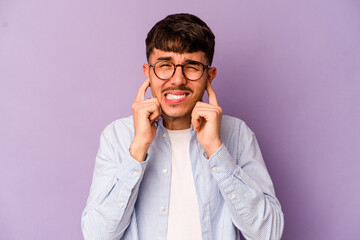 Young caucasian man isolated on purple background covering ears with hands.