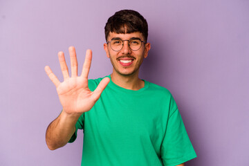 Fototapeta premium Young caucasian man isolated on purple background smiling cheerful showing number five with fingers.