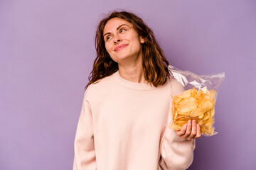 Young caucasian woman holding a bag of chips isolated on purple background dreaming of achieving goals and purposes