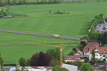Krankenwagen und Autos fahren über eine Landstraße mit grünen Feldern bei Hammelburg, Bad...