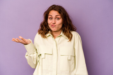 Young caucasian woman isolated on purple background doubting and shrugging shoulders in questioning gesture.