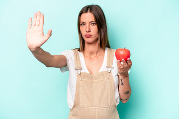 Young caucasian pregnant woman holding an apple isolated on blue background standing with...