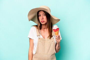 Young caucasian pregnant woman holding an ice cream isolated on blue background shrugs shoulders and open eyes confused.