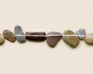 Top view still life with sea stones on sand background, pebbles united by one horizontal row. Seamless row from stone natural tones. Minimal style, concept of calm, meditation, design element