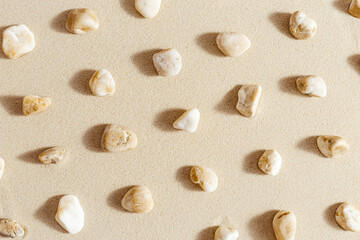 Fototapeta na wymiar Sea stones neutral beige color on natural fine sand background. Styled pattern from natural white yellow pebbles, monochrome tones. Spa minimal background