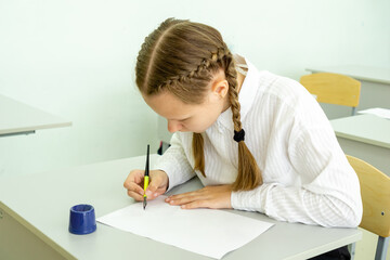 Naklejka na ściany i meble A cute schoolgirl kid sitting at a school desk and writes in her notebook. Back to school education concept. . High quality photo