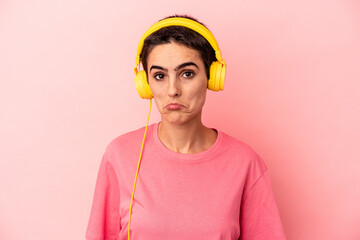 Young caucasian woman listening to music isolated on pink background shrugs shoulders and open eyes confused.