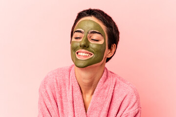 Young caucasian woman wearing a face mask isolated on pink background laughing and having fun.