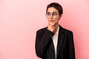 Young business woman isolated on pink background looking sideways with doubtful and skeptical expression.
