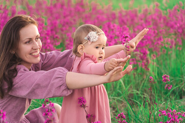 A happy mother with a child daughter aged two years have fun in a meadow with purple blooming flowers