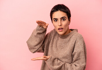 Young caucasian woman isolated on blue background shocked and amazed holding a copy space between hands.