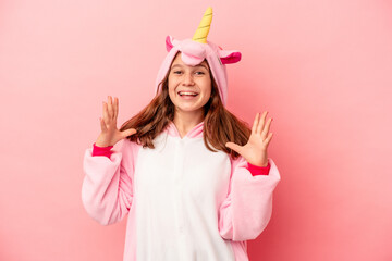 Little caucasian girl wearing a unicorn pajama isolated on pink background receiving a pleasant...