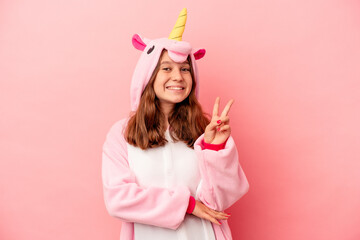 Little caucasian girl wearing a unicorn pajama isolated on pink background showing number two with...