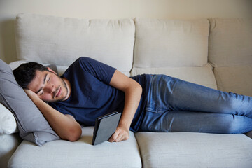 Young man lying asleep reading in an ebook on the sofa
