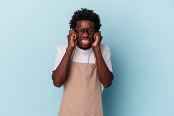Young african american store clerk isolated on blue background covering ears with hands.