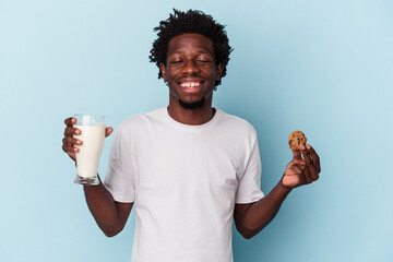Young african american man eating chocolate chips cookies and drinking milk on blue