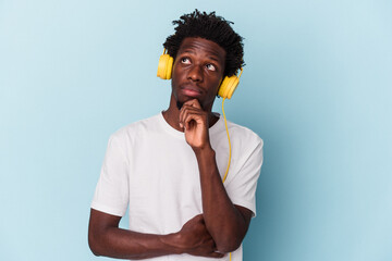 Young african american man listening to music isolated on blue background looking sideways with...