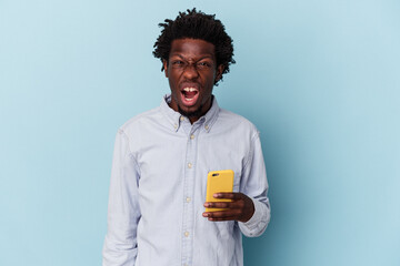 Young african american man holding mobile phone isolated on blue background screaming very angry and aggressive.