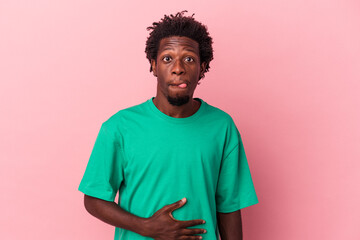 Young african american man isolated on pink background touches tummy, smiles gently, eating and satisfaction concept.