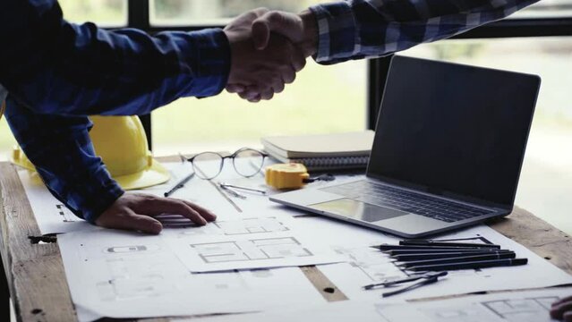 Two Civil Engineer or Architect holding helmet and handshaking after a mega project done in the office construction site. engineer sketching a construction project teamwork and cooperation concept. 4k