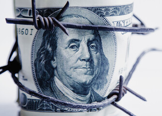 Economic warfare, sanctions and embargo busting concept. US Dollar money wrapped in barbed wire. Close up.