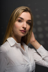 A young pretty girl in a white blouse. Close-up portrait on a gray background. Long blonde hair. Big brown eyes. A place for text advertising