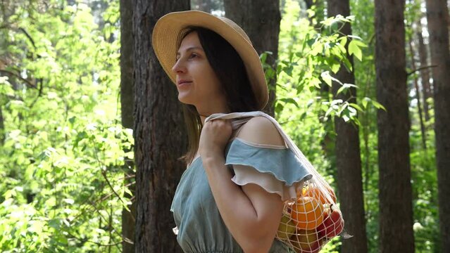 Woman walks with a braided string bag of fresh fruit. Life without plastic waste. Low-waste lifestyle. Sustainable ecological lifestyle