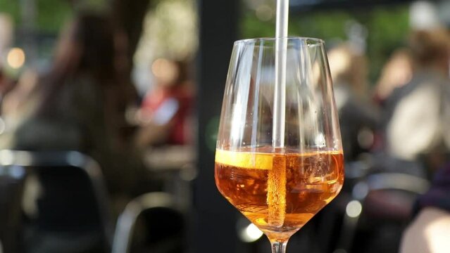 Ein Glas Mixgetr&auml;nk Cocktail Spritz mit Strohhalm in einem Biergarten im Sommer