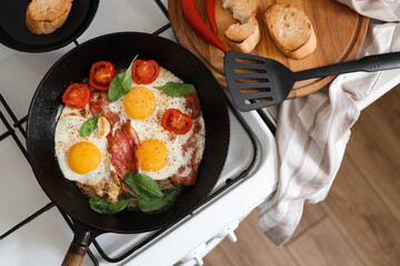 Delicious fried eggs with bacon and tomatoes in pan on stove, top view - obrazy, fototapety, plakaty