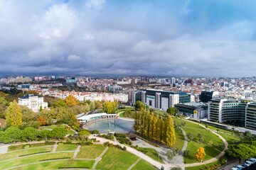 Fototapeta na wymiar Aerial view of observation deck of Parque Eduardo VII or Park of Eduard the VII Sloped, scenic park featuring tree-lined walking paths, manicured lawns & distant water views in Lisbon 