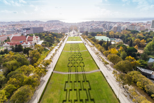 Aerial view of observation deck of Parque Eduardo VII or Park of Eduard the VII Sloped, scenic park featuring tree-lined walking paths, manicured lawns & distant water views in Lisbon 