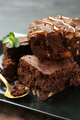 Delicious chocolate brownies with nuts, caramel sauce and fresh mint on plate, closeup