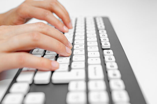 Female hands are typing on a white keyboard of a personal computer.