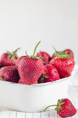 Red strawberries in a white square bowl on a white background..