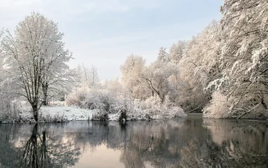 Foto auf Leinwand Snow-covered trees covered with frost on the riverbank in winter © Denis Shitikoff