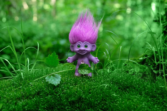 cute tale troll in forest, mossy natural green background. troll toy with ruffled violet hair in mystery forest, symbol of fairytale. magic atmosphere