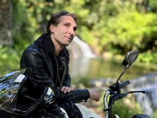 Fototapeta na wymiar a man sitting on a motorcycle against the backdrop of the nature of Portugal he dreams and looks up he has very kind deep eyes, dark hair and a black leather jacket, he is 35-45 years old.