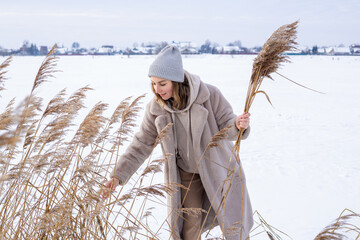 A young woman in a beige dress of neutral colors collects pampas grass. 