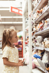 Little caucasian girl choosing a new toy in the big baby store. Big shelfs full of toys