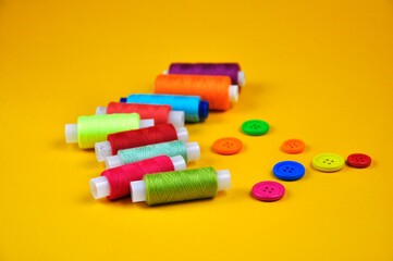 Set of buttons and Spools with multicolored threads on a yellow background. Blurring background.