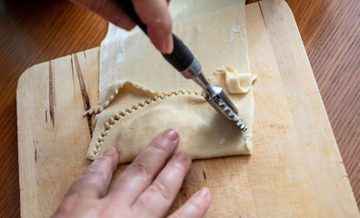 Kalitsounia Cretan traditional pies. Hand with a pastry wheel cut homemade dough, close up.