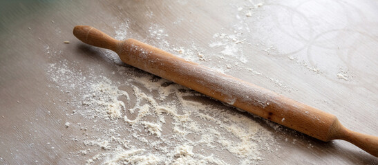 Homemade dough and pastry on kitchen table. Rolling pin, dough roller and flour on wood, close up