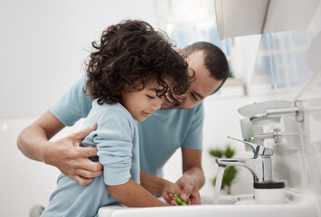 We brush now, and then later tonight again. Shot of a father helping his son rinse his toothbrush...