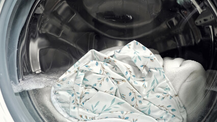 White laundry in washing machine with clear water and white foam. Clean water with small bubbles makes foam and soaks used bed linen closeup