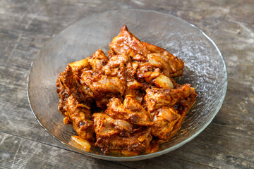 Pieces of chicken in sauce fried in a glass plate on a dark wooden table.