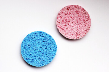 Pink and blue round textured cosmetic sponges on white background, horizontal photo. Beauty accessory for skincare, face makeup cleaning, frontal view