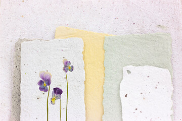 Dried viola flower pressed onto a sheet of handmade paper with a pronounced explicit texture. Reuse...